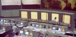 Overall view of the Mission Control Center (MCC), Houston, Texas, during the Gemini 5 flight. Note the screen at the front of the MCC which is used to track the progress of the Gemini spacecraft.
