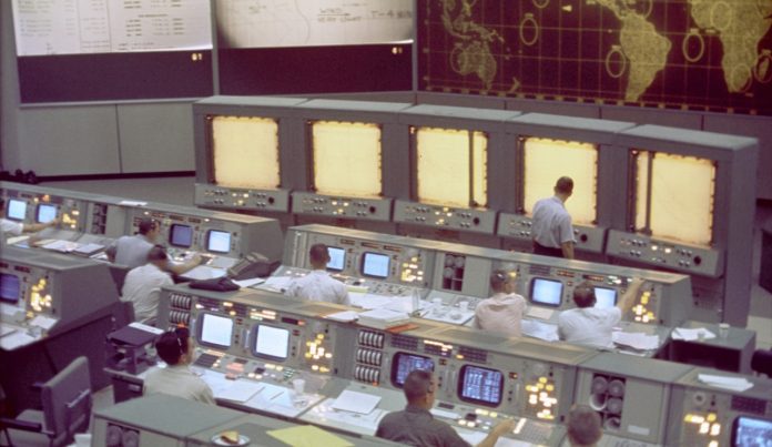 Overall view of the Mission Control Center (MCC), Houston, Texas, during the Gemini 5 flight. Note the screen at the front of the MCC which is used to track the progress of the Gemini spacecraft.