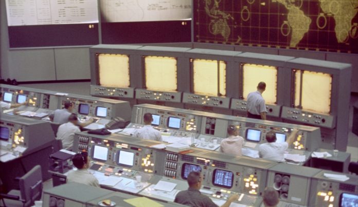 Nasa Overall view of the Mission Control Center (MCC), Houston, Texas, during the Gemini 5 flight. Note the screen at the front of the MCC which is used to track the progress of the Gemini spacecraft.